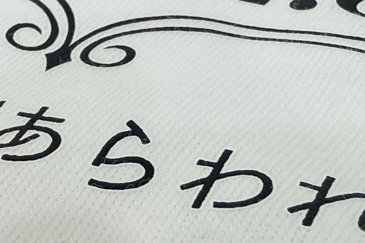 フルカラー転写（DTF）プリントの拡大写真。白いボディに黒い文字を転写し、文字の周りにボディと同色（白）のフチ（塗り足し）がついている
